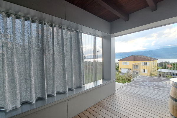Coolish Hitzeschutz: Speziell Sonnenlicht reflektierende Vorhänge mit Silberbedampfung für die Ausstattung moderner Balkone und Terrassen. Innenansicht einer Loggia mit silber-metallisierter Coolish Outdoor-Vorhang-Front zur Hitze-Reflexion.