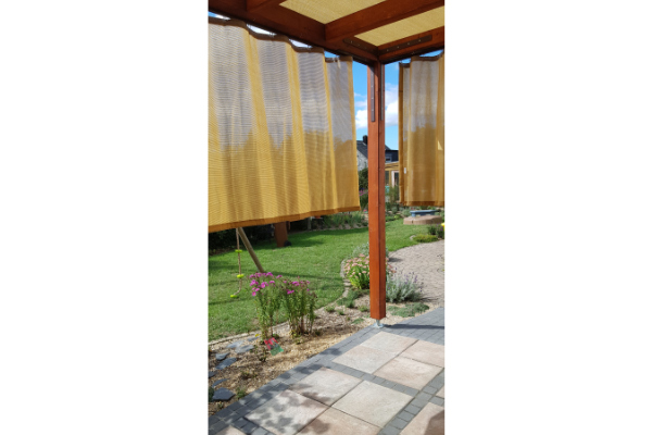 Nahaufnahme des hellen HDPE-Vorhangstoffs Fresh an einer Holzpergola mit Blick in den Garten