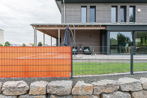 Sichtschutznetz 140 - schnell an jedem Zaun befestigt Sichtschutznetz 140 in orange vor der Terrasse eines modernen Holzhauses