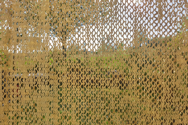 Atmosphärischer Sichtschutz: Camouflage-Vorhang nach Maß mit hoher Lichtdurchlässigkeit und Durchlüftung. Semi-transparenter Outdoor-Vorhang Camouflage in Beige vor Gartenkulisse mit natürlichem Lichtspiel durch die offene Gewebestruktur.