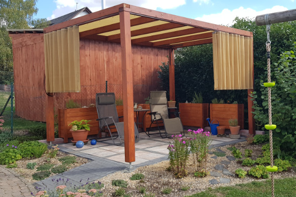Teilweise geöffnete Terrassenvorhänge auf halber Höhe an einer Pergola bieten flexiblen Blendschutz und freie Sicht