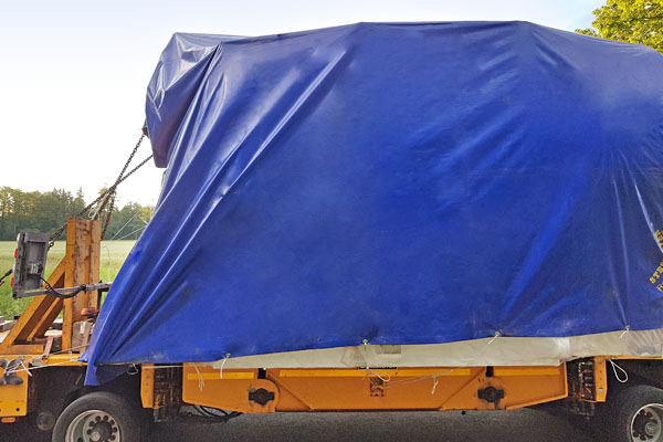 PVC-Planen sind belastbar und werden auch als Transportplane eingesetzt. Wichtig ist wegen dem Fahrtwind eine sichere Verspannung. PVC-Plane in blau auf dem Tieflader eines LKW als Transportplane verspannt und somit gegen den Fahrwind gesichert.