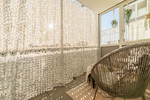 Wohlfühlatmosphäre auf dem Balkon: Camouflage-Vorhang mit exklusivem Licht- und Schattenspiel. Heller Balkon mit montiertem Outdoor-Vorhang Camouflage nach Maß und markantem Schattenmuster auf dem Boden durch einfallendes Sonnenlicht.